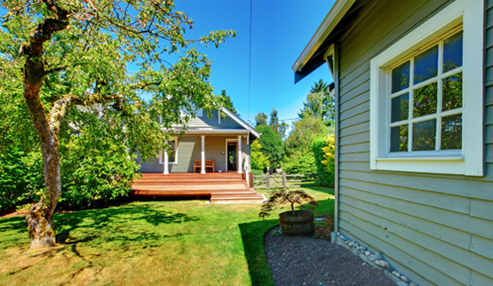 Photograph of the front façade of a detached accessory building, with a tree, lawn, and side façade of the primary building in the foreground.