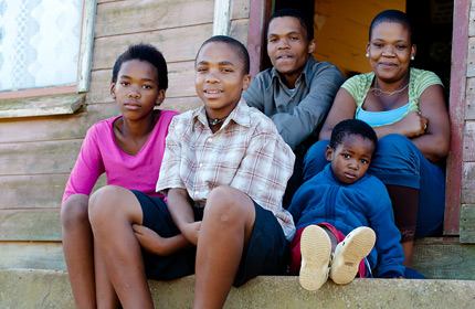  Photograph of a man, a woman, and three children sitting on the concrete steps and in the doorway to house with wooden siding.