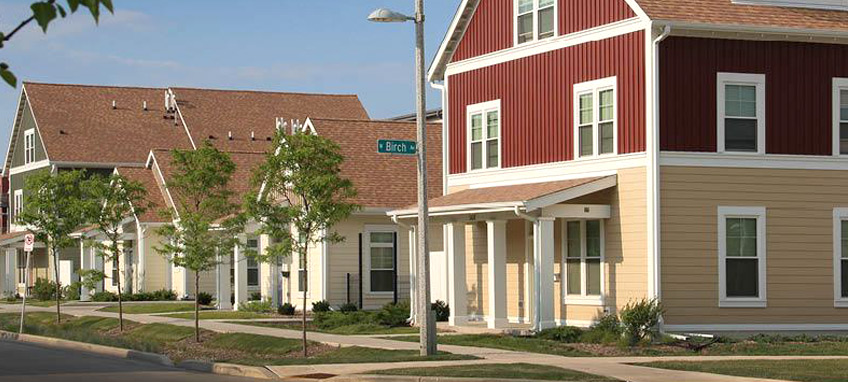 Multi-story and single-story buildings with porches along a tree-lined street with sidewalks.