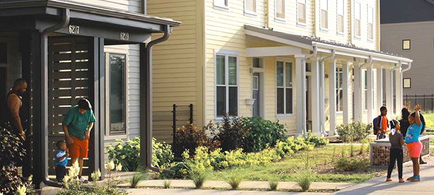 Children gathering in front of two-story, attached residential units with porches. 