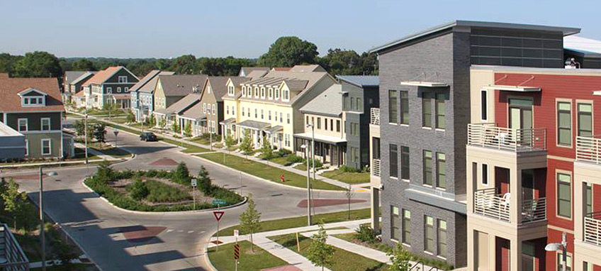 A photograph of a neighborhood showing several street-facing residential buildings, as well as a network of sidewalks and streets with a traffic circle in the center.