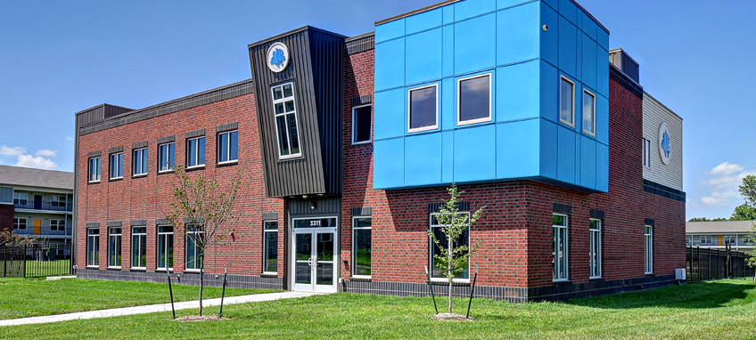 Photo of the front and side facade of a two-story red brick building with distinctive contrasting projections on the second floor. 