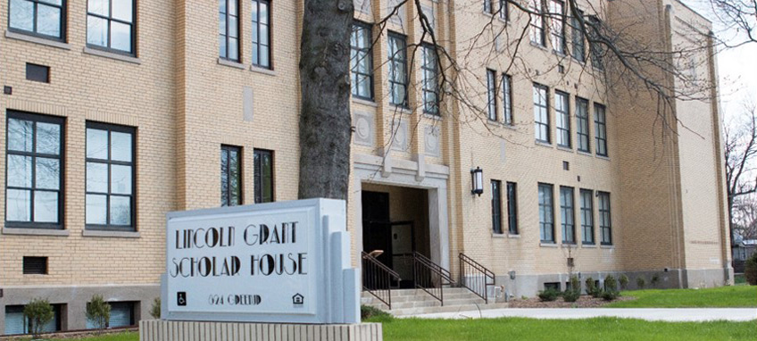 Photo of the facade of a three-story pale brick building labeled with a sign that reads "Lincoln Grant Scholar House".