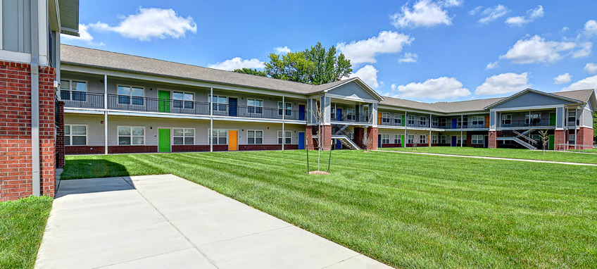 Photo of a U-shaped multifamily residential building with first- and second-floor units built around a grassy courtyard. 