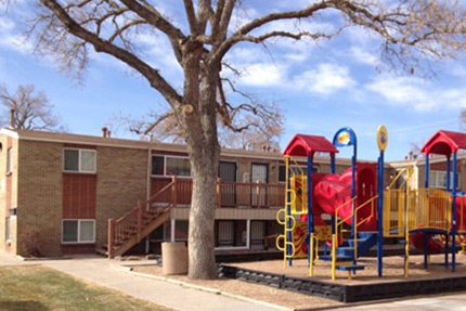 Photograph of multiple two-story residential buildings located adjacent to a small playground. 