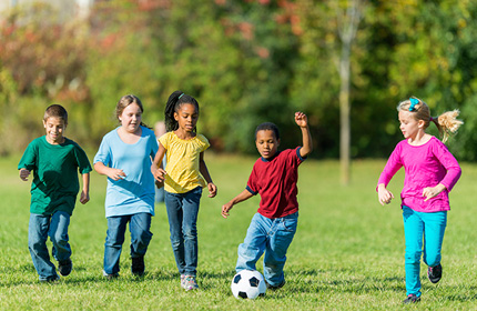 Photograph of five children, three girls and two boys, playing soccer in a field.