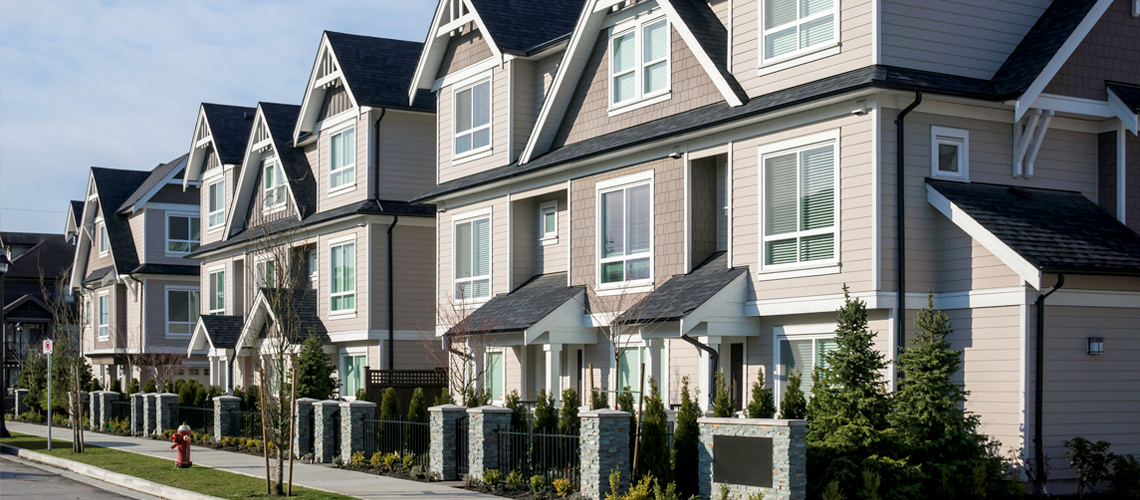 Photograph of three-story townhouses with siding facades along a street. Featured article