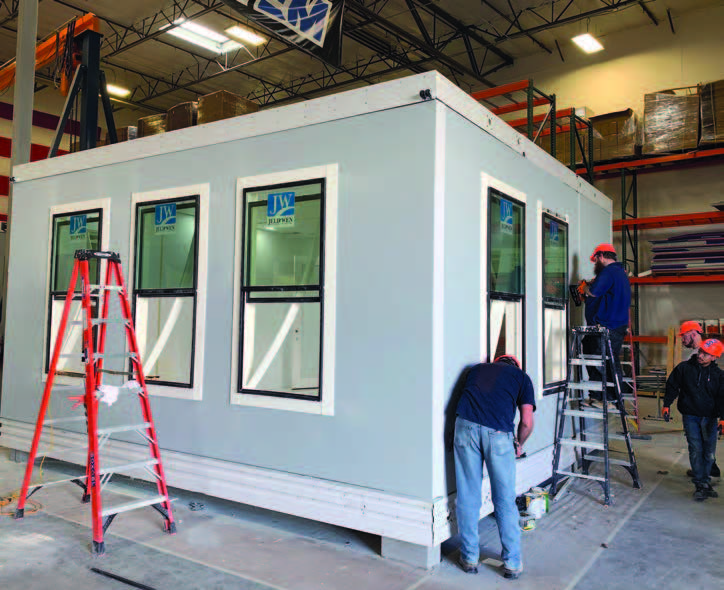 Photo shows three men working on an accessory dwelling unit being constructed inside a factory.