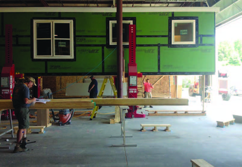 Three men work on a modular home under construction inside a building.