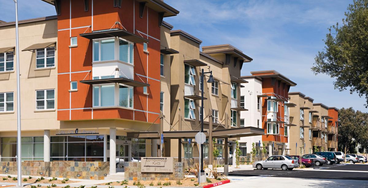 Photo shows front and side facades of three-story apartment buildings within a complex.