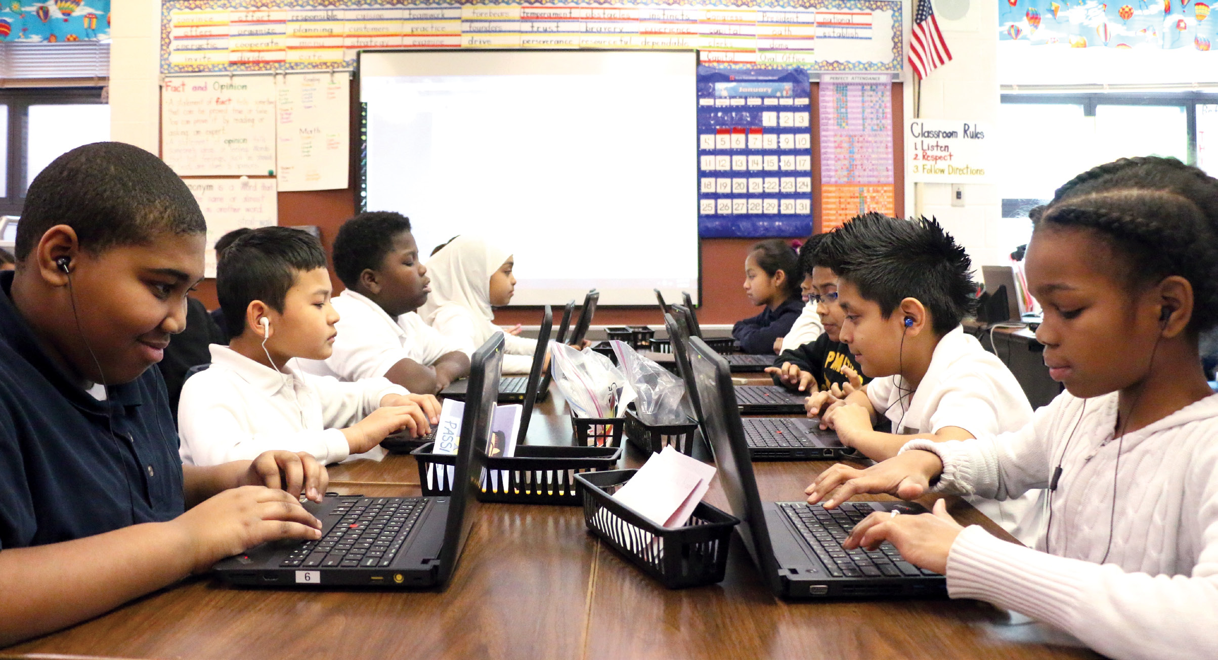 Children sitting across from each other and working on laptop computers in a classroom.