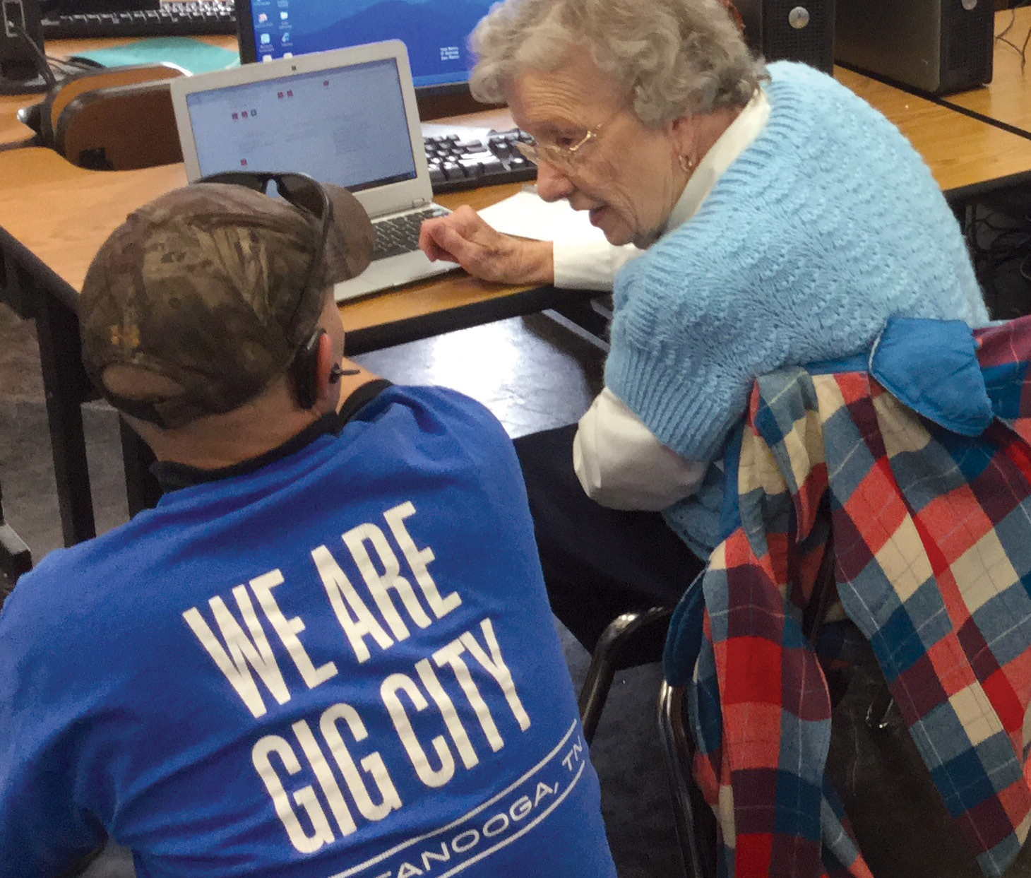 A volunteer assisting an older woman working on a laptop computer.