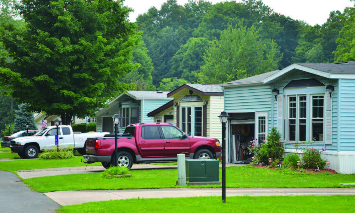 Angled front view of three homes in a manufactured home park with vehicles parked in the driveways.