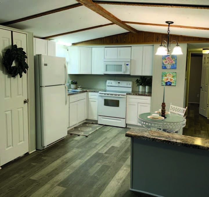 Interior view of a manufactured home showing an open kitchen with refrigerator, microwave, and range.
