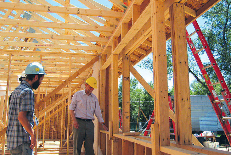 Photo shows a wood-frame building with double-stud walls and two men in hard hats.
