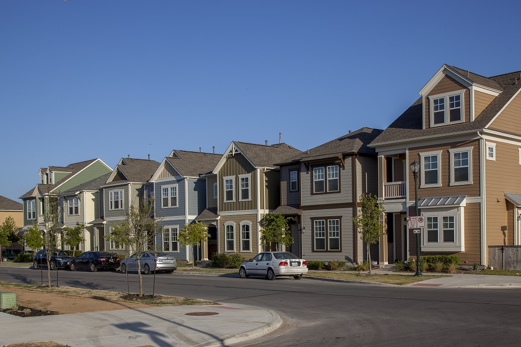 A row of closely-spaced single-family homes with three cars parked on the street.