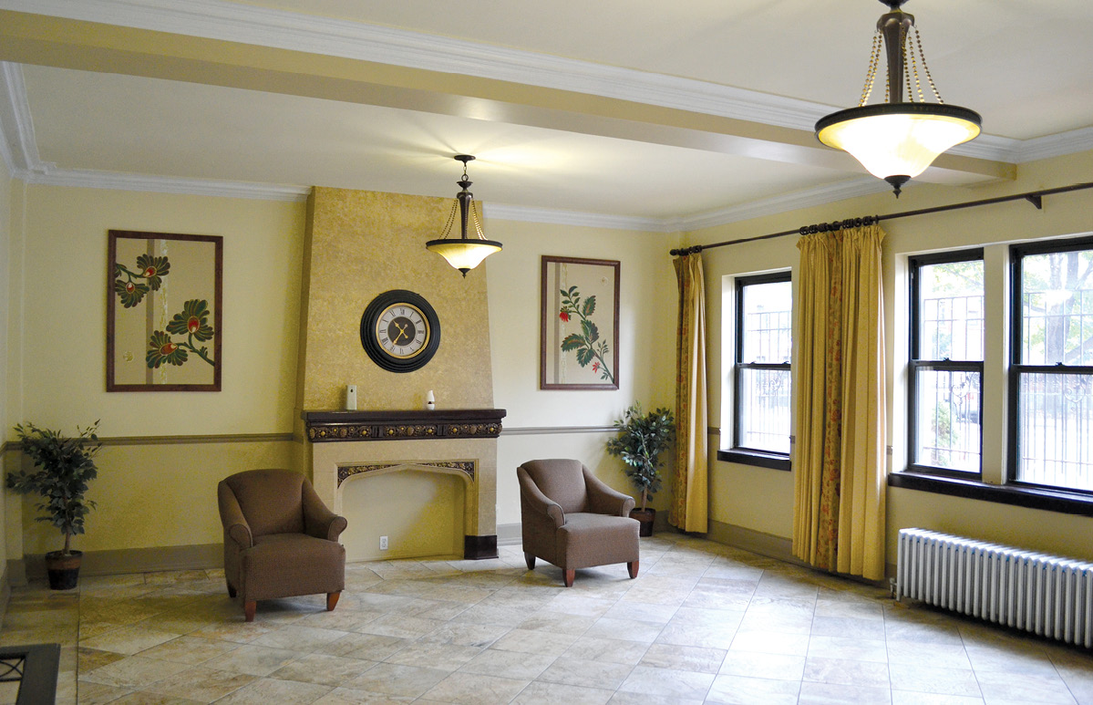 Two arm chairs are seen in a room with two chandeliers and windows along one wall.