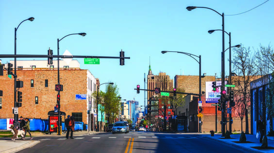 An urban neighborhood with buildings, street lamps, cars, and pedestrians.