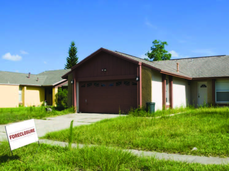 View of a vacant house with a foreclosure sign in the front yard.