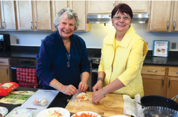 Two women stand next to each other in a kitchen cutting vegetables.