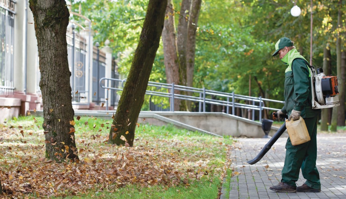 A man standing on a sidewalk using a leaf blower.