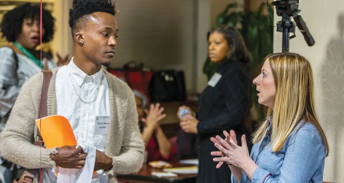 A man listening to a woman in a job fair setting.