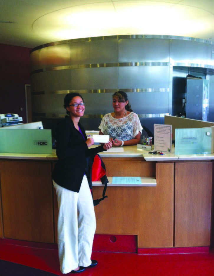 A young woman stands at a bank counter with a check in her hand.