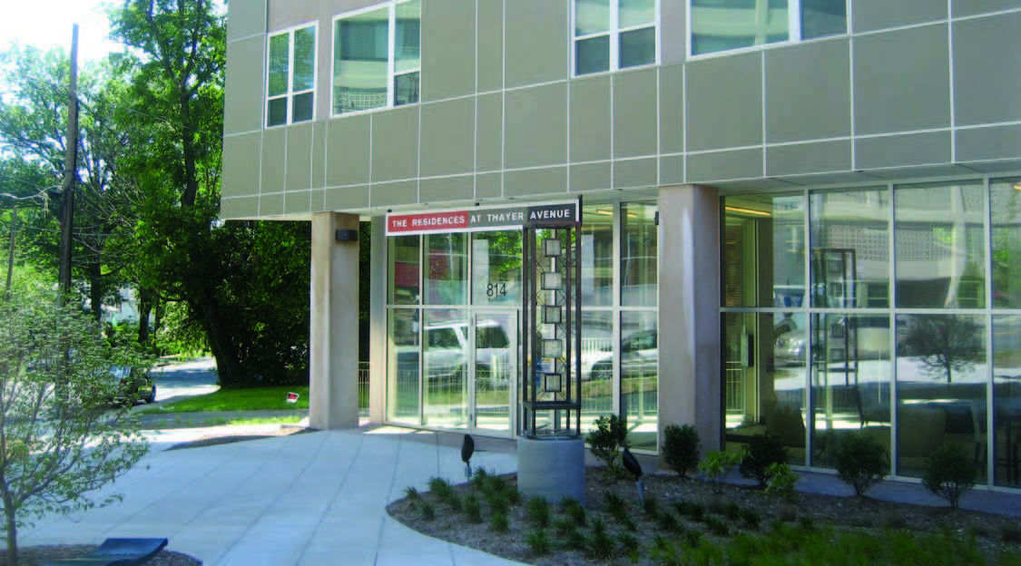 Photo shows glass-walled entrance and ground floor of a multistory residential building.