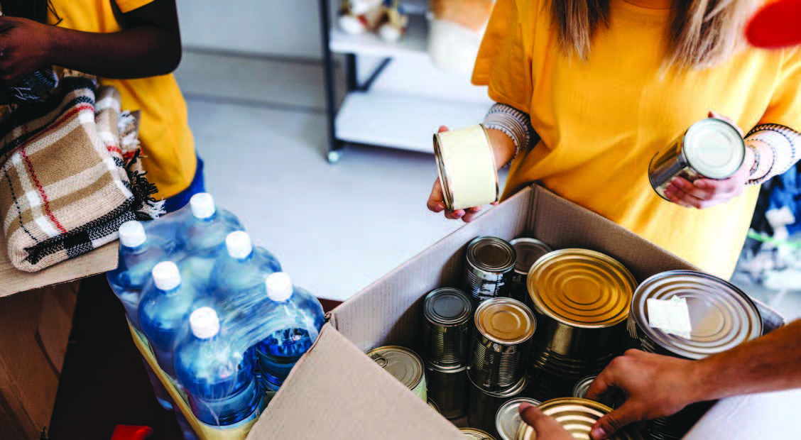 Three individuals packing canned goods into a cardboard box.