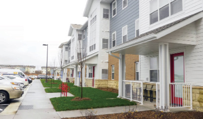 A three-story multifamily building with sidewalk and cars in the front.