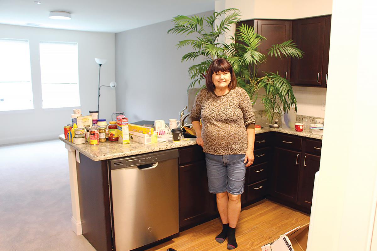 A woman stands next to a dishwasher in a kitchen with food items on the counter.