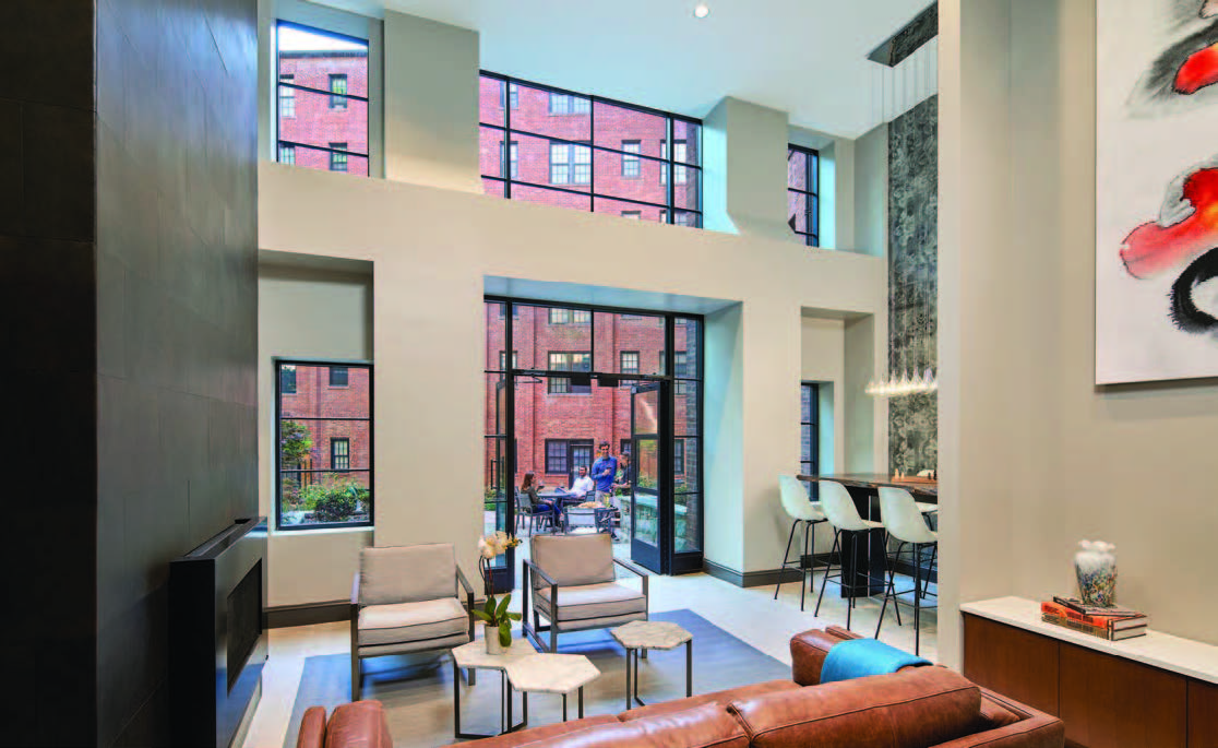 Photo of interior of a two-story common room with different types of seating and glass doors opening to a courtyard area where four people are socializing.