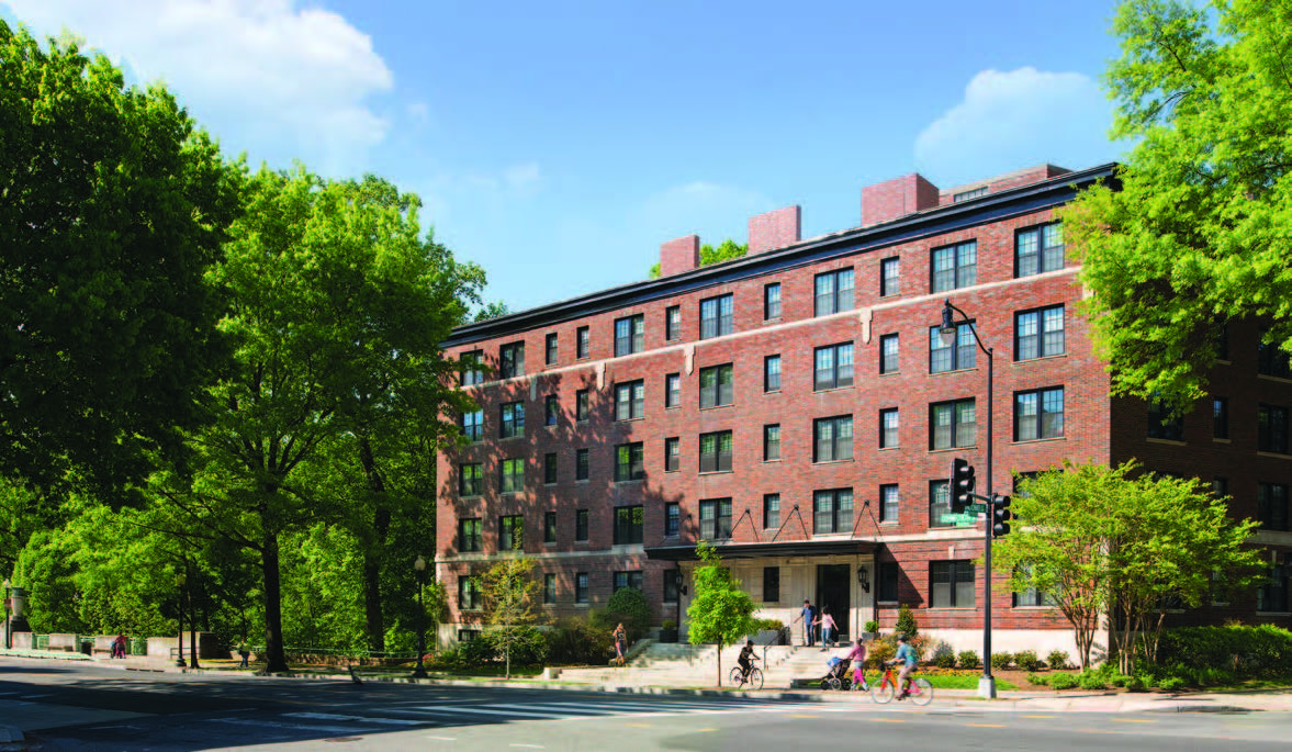 Photo of front façade of a five-story building with people exiting the building and biking on sidewalk in front of the building.