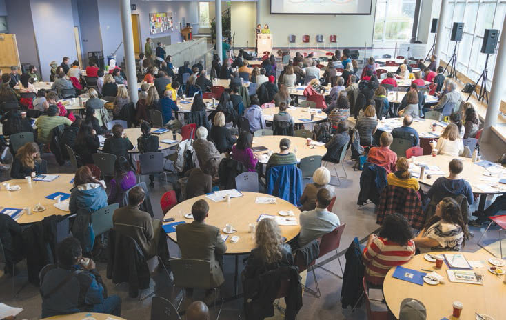 A photo showing community residents seated at round tables participating in a planning meeting.