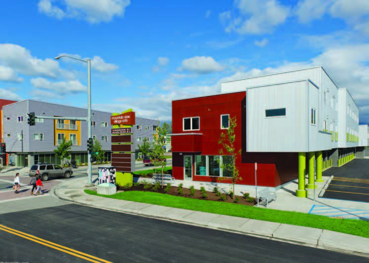 Photo shows two buildings located at crossroads with retail on the first floor and housing above.