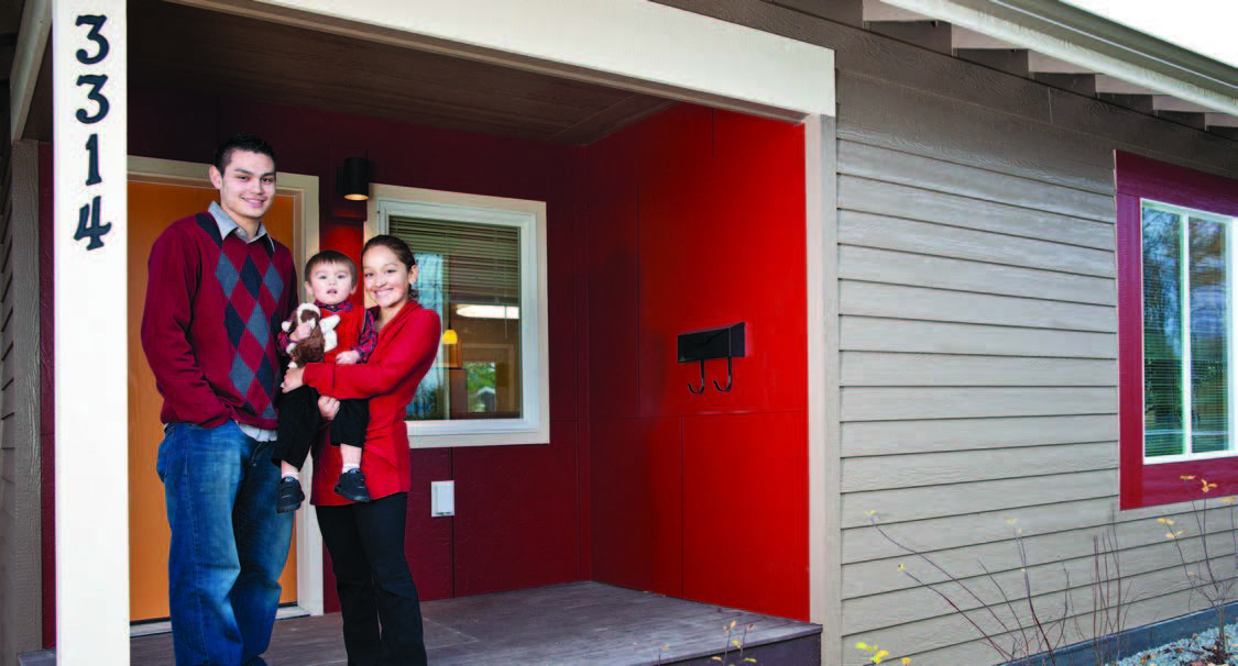 A young couple holding their son is standing on the front porch of their new home.