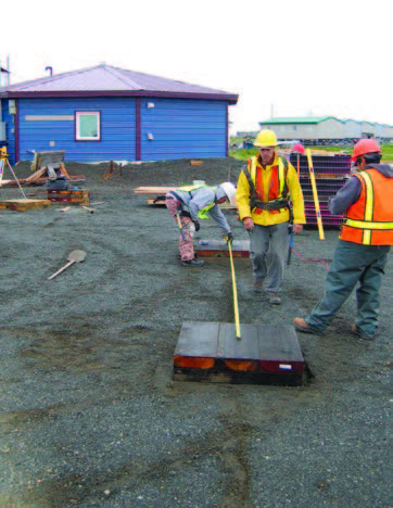 Photo shows a construction site with men in hard hats and the Quinhagak prototype house in the background.