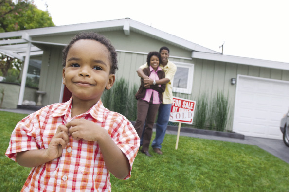 A little boy and his parents stand smiling in front of their new home.