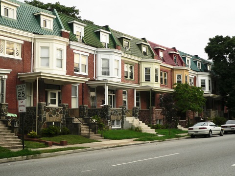 Photograph displaying a row of townhomes with similar façades facing a street. 