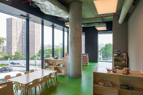 Photograph of the interior of a classroom with large windows overlooking an urban street.