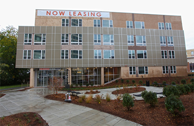 Photograph of the side facade of a four-story multifamily apartment building with a sculpture garden in the foreground.