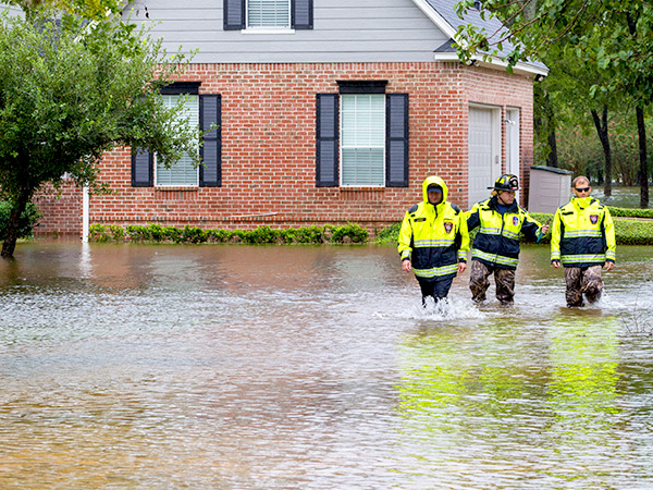 Three emergency responders wade through floodwater next to a residence. 