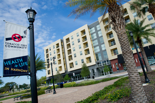 Photograph of a multi-story building, surrounded by a courtyard and palm trees. A sign stating, “Tobacco-Free Community,” is visible in the foreground.