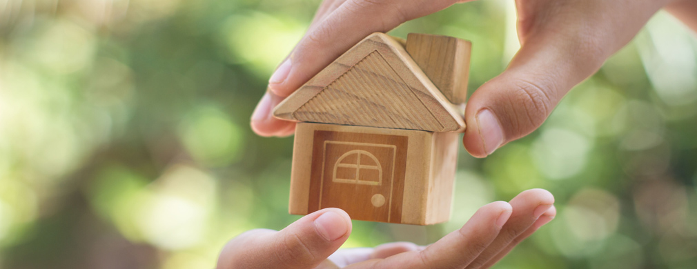 The hand of someone giving a model house to someone else's hand.