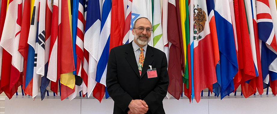 Deputy Assistant Secretary Kurt Usowski in front of flags at the OECD building.