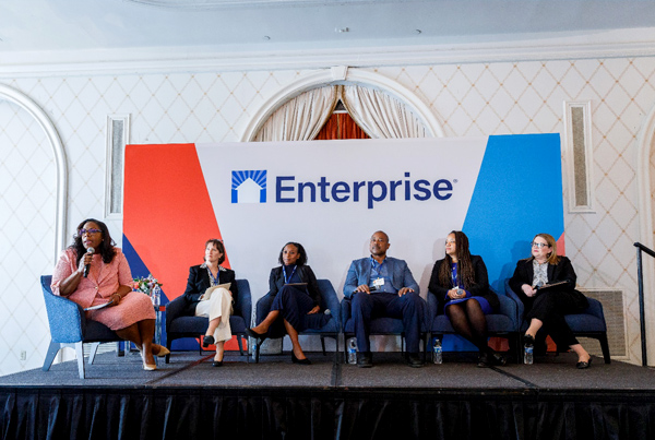 Panelists sitting in chairs on a platform, and a large poster behind them with the text 'Enterprise'.
