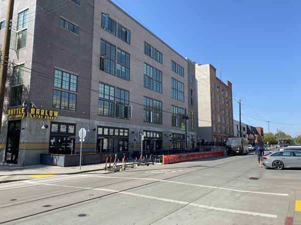 Photograph of the exterior of a four-story building and a road with a crosswalk and street parking. 