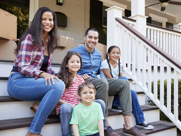 Photo of a family sitting on the front steps of a house with boxes behind them.