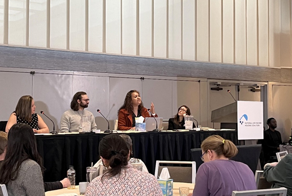 Four panelists sit at a table with the audience in the foreground.