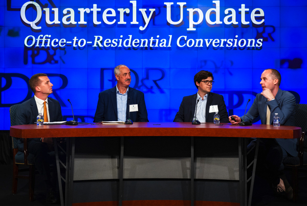 Four panelists sitting at a table with a screen behind them that reads "Quarterly Update Office-to-Residential Conversions"